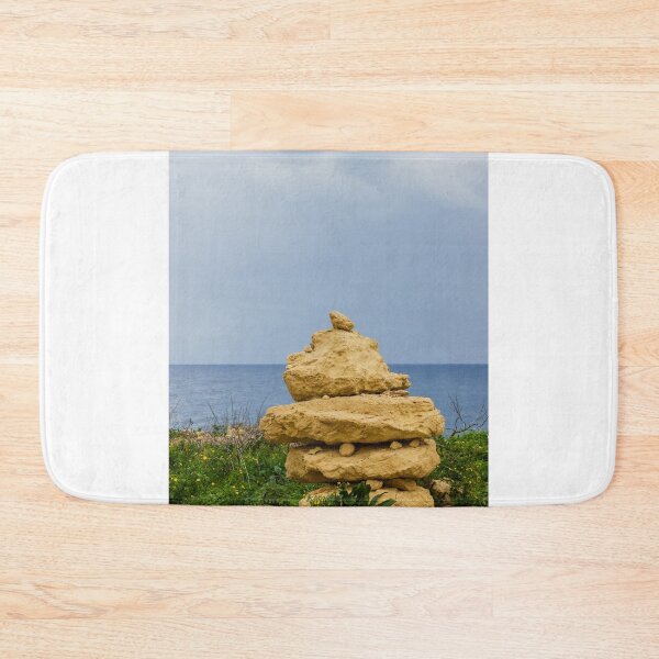 Item preview, Stacked Coastal Rocks Beside Calm Sea Under Cloudy Sky With Green Vegetation And Wildflowers designed and sold by Nmallia.