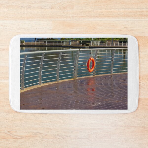 Item preview, Orange Lifebuoy Hanging on Metal Railing Along Waterfront Boardwalk Promenade Over Calm Harbor Water designed and sold by Nmallia.
