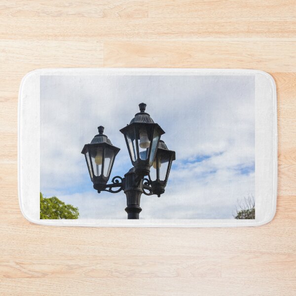 Item preview, Vintage Three-Head Street Lamp Lantern On Decorative Lamppost Against Blue Cloudy Sky designed and sold by Nmallia.
