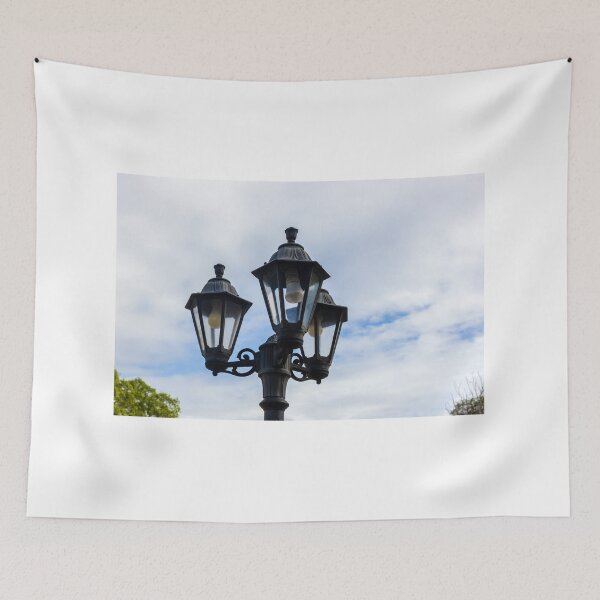Item preview, Vintage Three-Head Street Lamp Lantern On Decorative Lamppost Against Blue Cloudy Sky designed and sold by Nmallia.