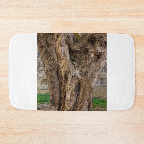 Item preview, Old Gnarled Tree Trunk With Weathered Bark Texture Against Stone Wall In Garden Setting designed and sold by Nmallia.