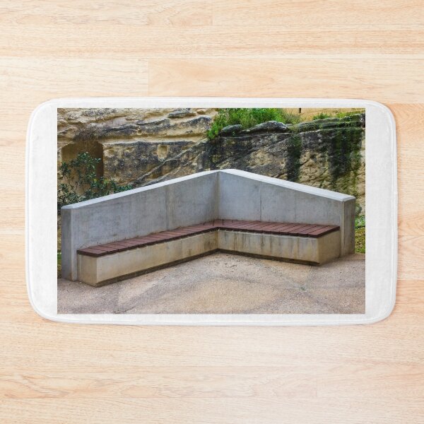 Item preview, Concrete Corner Bench With Wooden Slats Against Weathered Rock Wall In Outdoor Park designed and sold by Nmallia.