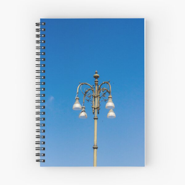 Item preview, Ornate Vintage Street Lamp Against Bright Blue Sky With Elegant Metalwork and Hanging Lights designed and sold by Nmallia.