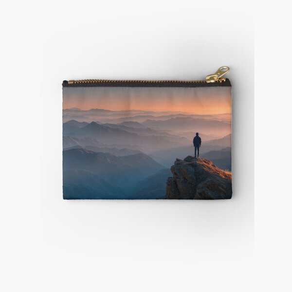 Item preview, Majestic Mountain Peak Sunset Hiker Silhouette Wall Art Standing Above Misty Horizon Landscape Photography Print in Golden Hour Orange and Misty Blue Tones designed and sold by SurfaceCraft Studio.
