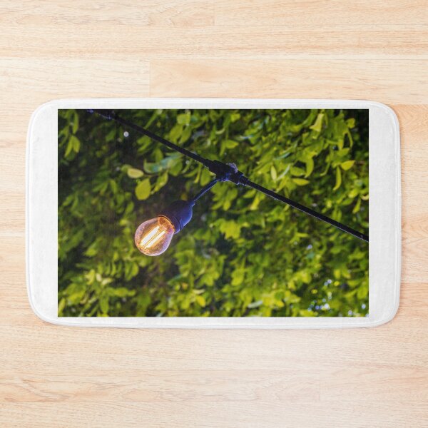 Item preview, Warm Glowing Light Bulb Hanging From Outdoor String Lights Over Lush Green Garden Foliage designed and sold by Nmallia.
