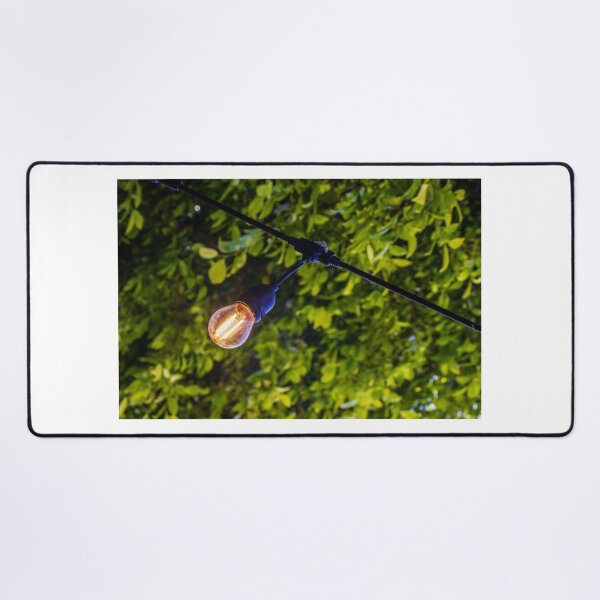 Item preview, Warm Glowing Light Bulb Hanging From Outdoor String Lights Over Lush Green Garden Foliage designed and sold by Nmallia.
