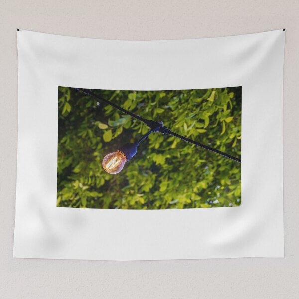 Item preview, Warm Glowing Light Bulb Hanging From Outdoor String Lights Over Lush Green Garden Foliage designed and sold by Nmallia.