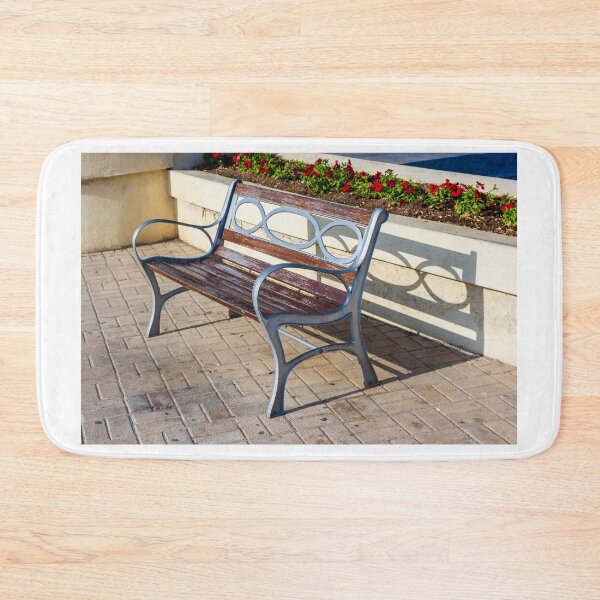 Item preview, Wooden And Metal Park Bench Casting Shadow Along Flowerbed On Sunny Pavement designed and sold by Nmallia.