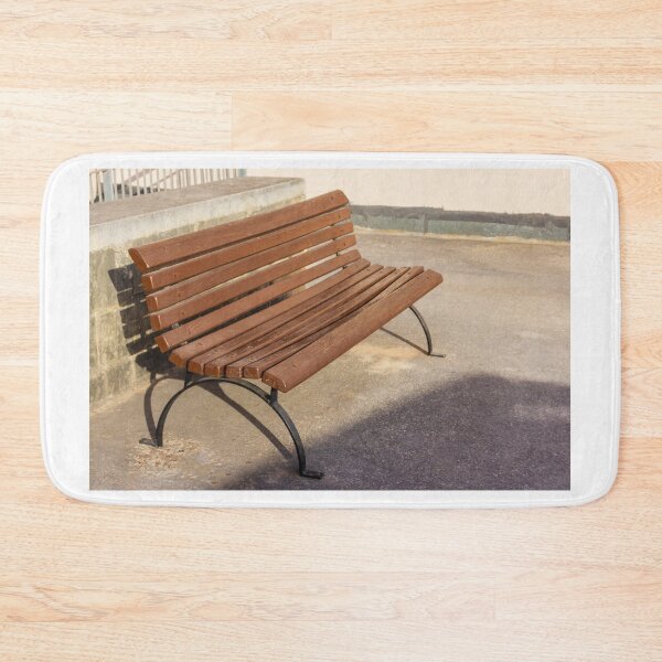 Item preview, Empty Wooden Bench in Sunlit Urban Park Beside Stone Wall on Asphalt Walkway Outdoor Seating designed and sold by Nmallia.
