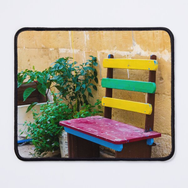 Item preview, Colorful Wooden Bench Against Textured Yellow Wall in Sunny Courtyard With Green Plants designed and sold by Nmallia.