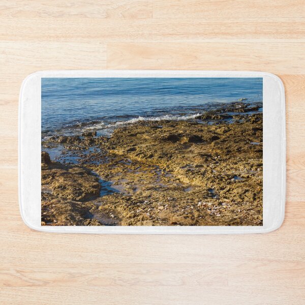 Item preview, Rugged Coastal Rocks By Calm Blue Water With Weathered Stone Pier And Small Post designed and sold by Nmallia.