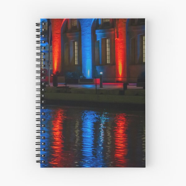 Item preview, Nighttime Waterfront Building With Red And Blue Illuminated Arches And Reflections On Water designed and sold by Nmallia.