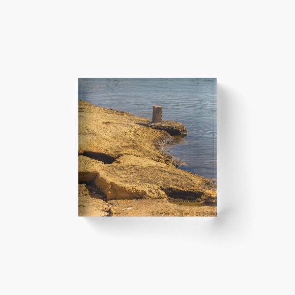Item preview, Rugged Coastal Rocks By Calm Blue Water With Weathered Stone Pier And Small Post designed and sold by Nmallia.