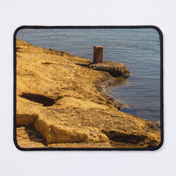 Item preview, Rugged Coastal Rocks By Calm Blue Water With Weathered Stone Pier And Small Post designed and sold by Nmallia.