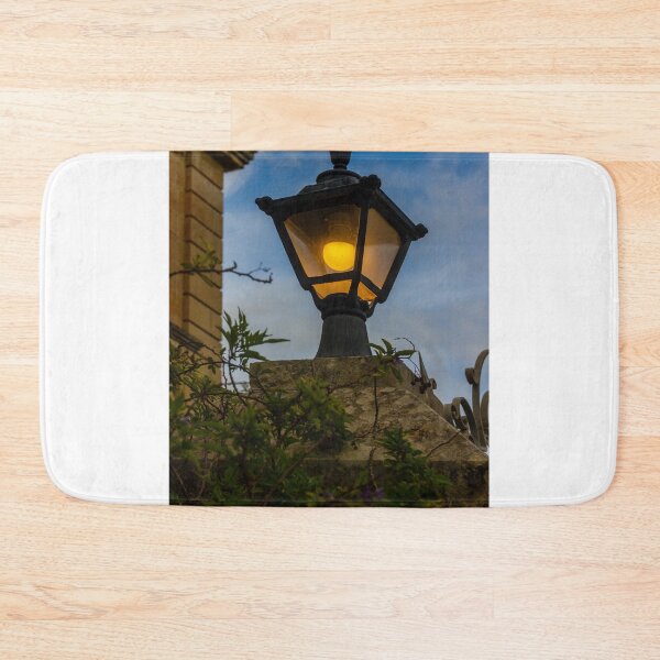 Item preview, Vintage Streetlamp With Warm Glow Over Stone Wall Amid Ivy And Evening Sky designed and sold by Nmallia.
