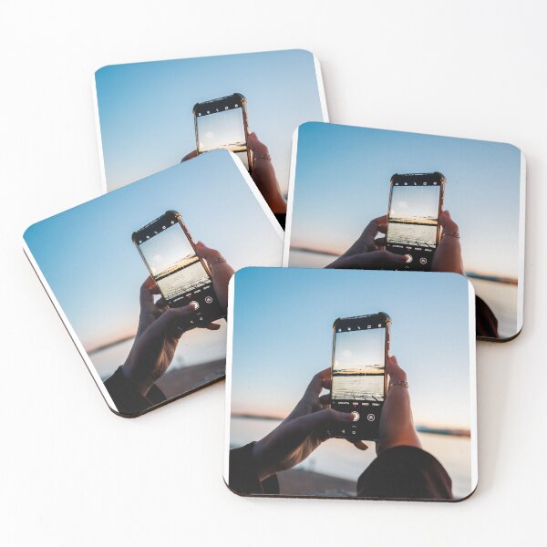 Item preview, Hands Holding Smartphone Capturing Sunset Over Water designed and sold by Kellesu.