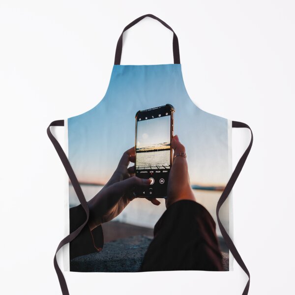 Item preview, Hands Holding Smartphone Capturing Sunset Over Water designed and sold by Kellesu.