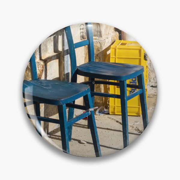 Item preview, Two Blue Chairs Against a Weathered Wall With Yellow Crate on Sunny Pavement designed and sold by Nmallia.