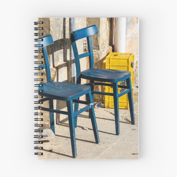 Item preview, Two Blue Chairs Against a Weathered Wall With Yellow Crate on Sunny Pavement designed and sold by Nmallia.