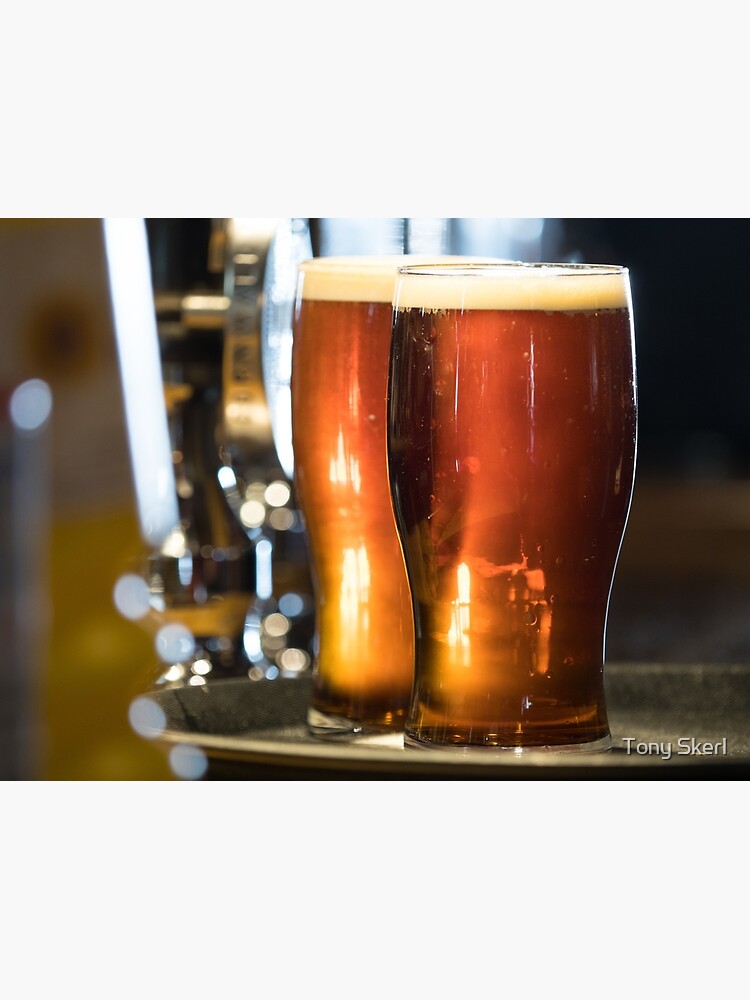 "Dark coloured ale stands on a tray in pint glasses back lit on a bar